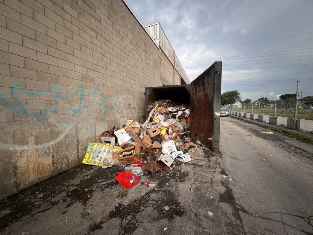Overflowing commercial compactor and loose waste before cleaning